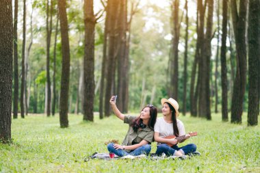 Ormanda ukulele oynarken selfie çeken iki kadın.