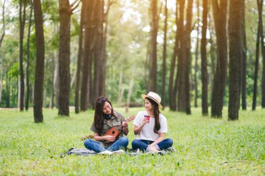 Ormanda birlikte otururken ukulele oynayan iki kadın.