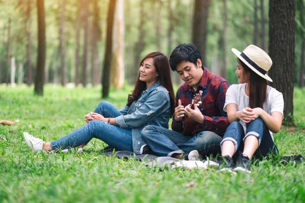 Parkta birlikte otururken ukulele oynayan bir grup genç.