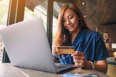 Güzel bir Asyalı kadın dizüstü bilgisayar kullanırken kredi kartı tutuyor.