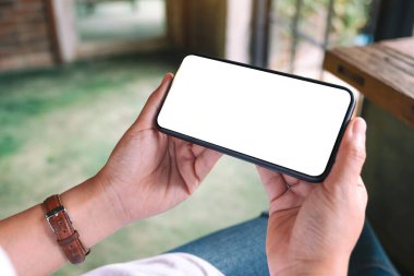 Kafede otururken elinde boş masaüstü ekran olan siyah cep telefonu tutan bir kadının görüntüsü