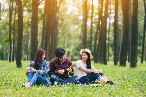Parkta birlikte otururken ukulele oynayan bir grup genç.