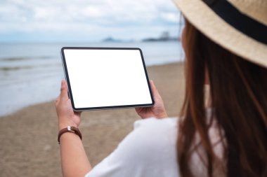 Deniz kenarında boş masaüstü ekranı olan siyah bir tableti tutan bir kadının görüntüsü.