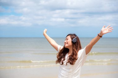 Deniz kenarında kulaklıkla müzik dinlerken kollarını açan güzel bir Asyalı kadın.
