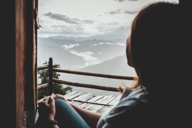 Sisli bir günde tek başına oturmuş dağları seyreden bir kadın.