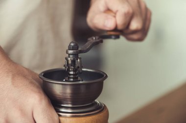 Kahve çekirdeğini öğütmek için eski ahşap kahve öğütücüsünü kullanan bir adamın ellerinin yakın plan görüntüsü.