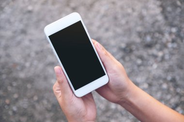 Sokak arkaplanlı, boş siyah ekranlı, beyaz cep telefonu tutan ellerin görüntüsü 