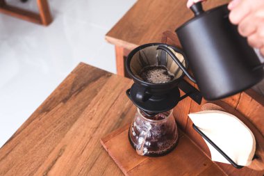 Eski ahşap masaya damlayan bir kahve yapmak için sıcak su döken bir elin yakın plan görüntüsü.