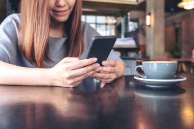 Elinde kahve fincanı olan akıllı bir telefonu tutan ve kullanan bir kadının yakın plan görüntüsü.