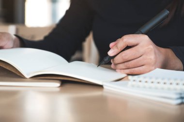 Tahta masaya boş defterler yazan bir kadının yakın plan resmi. 