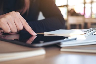 Siyah bir tablet bilgisayar ekranını işaret eden el resmi ve ahşap masadaki defter.