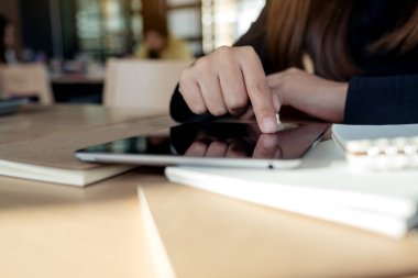 Siyah bir tablet bilgisayar ekranını işaret eden el resmi ve ahşap masadaki defter.