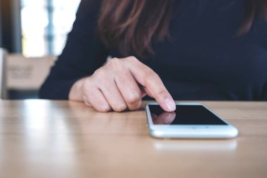 Ahşap masadaki bulanık arka planı olan akıllı telefonu kullanan ve dokunan bir kadın.