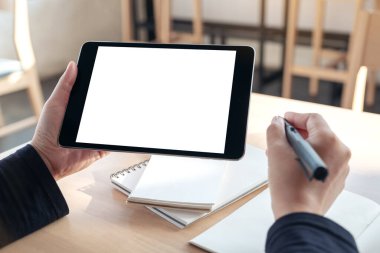 Ofisteki not defterlerine yazarken boş beyaz masaüstü ekran ile siyah tablet pc 'yi tutan ve kullanan ellerin görüntüsünü taklit et