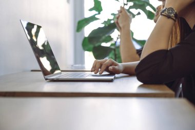 Ofiste iş arkadaşıyla birlikte çalışan ve dizüstü bilgisayarda klavyede yazan bir kadının yakın plan görüntüsü.