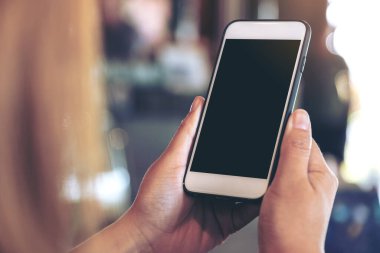 Boş siyah masaüstü ekranı ve bulanık arkaplanı olan beyaz cep telefonu tutan bir kadının görüntüsü