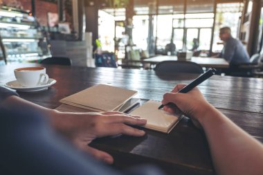 Kafedeki boş deftere yazı yazan bir kadının yakın plan resmi.