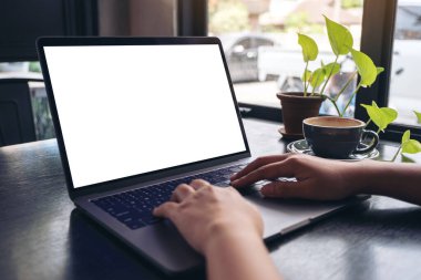 Bir kadının ellerinin boş beyaz masaüstü ekran ve kafeteryadaki ahşap masada kahve fincanı kullanırken ve daktilo yazarken görüntüsü.