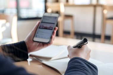 Çalışırken akıllı bir telefon ve kalem tutan ellerin yakın plan görüntüsü