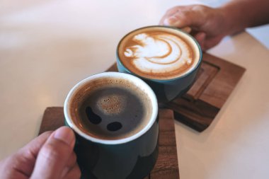 Kafede yeşil kahve fincanlarını tokuşturan bir kadın ve bir erkek resmi