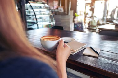 Kafe 'de elinde not defterleriyle sıcak kahve tutan ve içen bir kadının yakın plan görüntüsü.