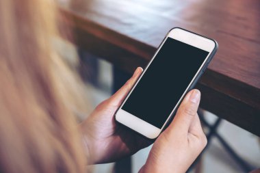 Boş siyah masaüstü ekranı ve bulanık arkaplanı olan beyaz cep telefonu tutan bir kadının görüntüsü