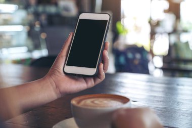 Modern kafede kahve içerken beyaz cep telefonunu boş ekran ile tutan ellerin görüntüsü.