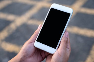 Sokak arkaplanlı, boş siyah ekranlı beyaz cep telefonlu el kamerası görüntüsü 