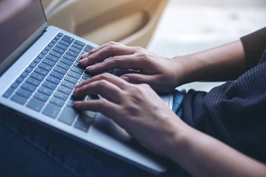 Kadının ellerinin kalçasındaki dizüstü bilgisayarda çalışırken ve yazarken yakın plan görüntüsü.