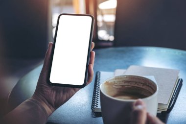 Antika kafede kahve içerken siyah cep telefonunu boş ekran ile tutan ellerin görüntüsü.