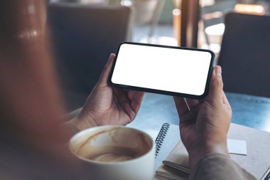 El ele tutuşmanın ve siyah bir cep telefonu kullanmanın görüntüsü. Masada kahve fincanı ile izlemek için yatay olarak boş ekran.