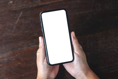 Tahta masa arkasında boş masaüstü ekranı olan siyah cep telefonunu tutan ellerin en üstteki görüntüsü