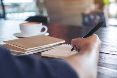 Kafe 'de kahve fincanı ile boş deftere yazan bir kadının yakın plan resmi.