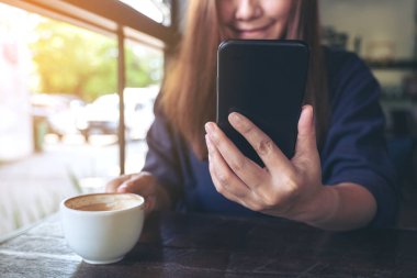 Kafede kahve içerken akıllı telefonu kullanan ve ona bakan Asyalı güzel bir kadının yakın plan görüntüsü.