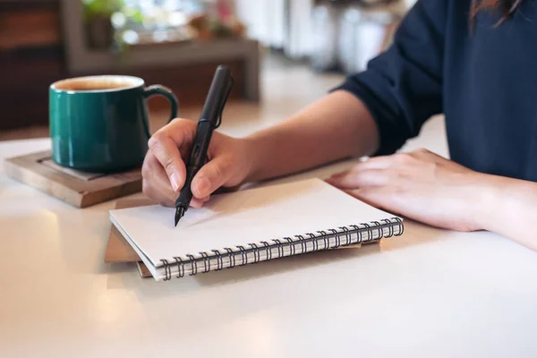 カフェのテーブルの上にコーヒーカップが置かれた空白のノートに女性の手の書き込みのイメージを閉じる — ストック写真