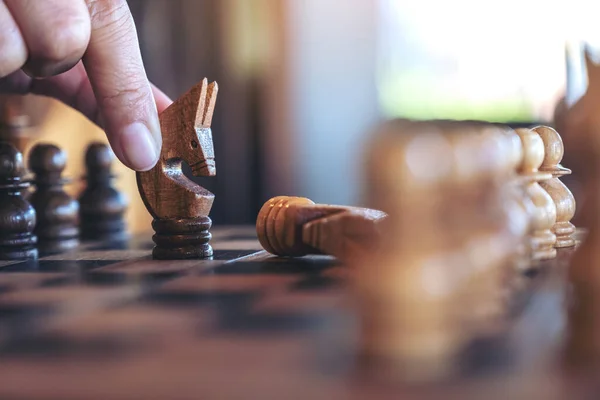 Closeup image of a hand holding and moving a horse to win another horse in wooden chessboard game