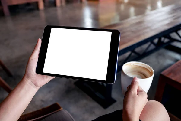 女性の手が黒いタブレットPcを持っているのモックアップ画像白い画面とカフェで木製のテーブルの上にコーヒーを飲みながら ストック写真