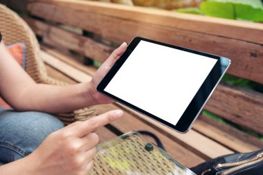 Açık havada otururken elinde siyah bir tablet olan beyaz ekranlı bir kadının görüntüsü.