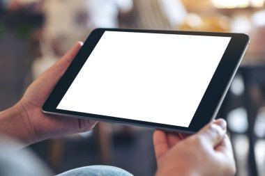 Kafede otururken elinde boş beyaz ekranlı siyah tablet tutan bir kadının görüntüsü.
