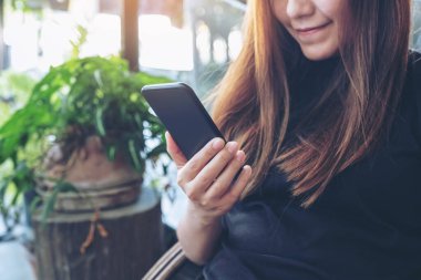 Asyalı bir kadının açık havada elinde tuttuğu, kullandığı ve baktığı akıllı telefonun yakın plan görüntüsü.
