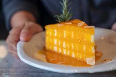 El ele tutuşup kafedeki seramik tabakta portakallı pastayı gösteren yakın plan.