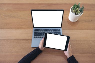 Üst görüntüde siyah tablet ve dizüstü bilgisayarla ofis masasında beyaz ekranlı ellerin görüntüsü var.