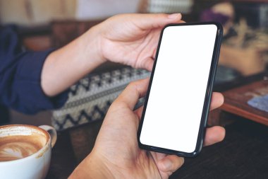 Kafe 'deki masada oturan birine elinde siyah bir cep telefonu tutan ve gösteren bir kadının görüntüsü.