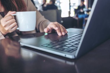Kafede kahve içerken bilgisayardaki dokunmatik dokunmatik ellerin yakın plan görüntüsü.