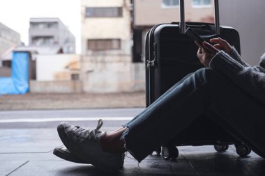 Kapalı çekim görüntüsü, seyahat etmek için siyah bavullu bir kadının oturduğu ve cep telefonu kullandığı.