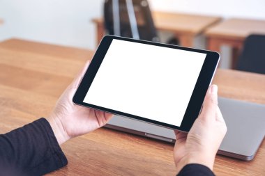 Ofisteki ahşap masadaki defter ile birlikte boş beyaz masaüstü ekranı olan siyah tablet bilgisayarın el ele tutuşunu ve kullanımını görüntüle