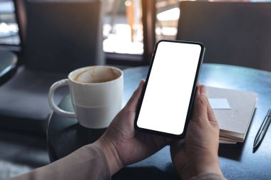 Elleri tutarken ve siyah bir cep telefonu kullanırken, boş ekran ile ahşap masada defter ve kahve fincanı kullanırken çekilmiş bir resim.