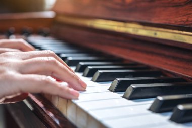 Kapalı çekimde, klasik ahşap bir piyanoyu çalan ellerin görüntüsü