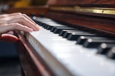 Kapalı çekimde, klasik ahşap bir piyanoyu çalan ellerin görüntüsü