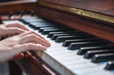 Kapalı çekimde, klasik ahşap bir piyanoyu çalan ellerin görüntüsü